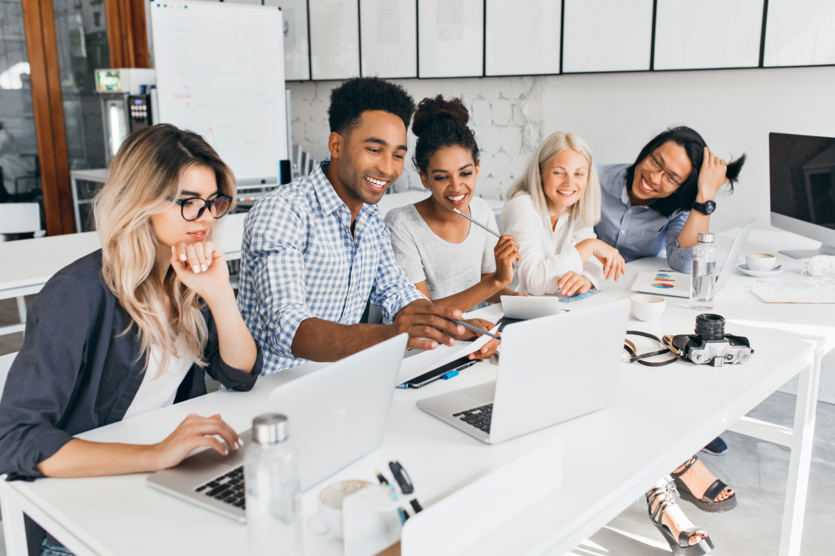 smiling-african-student-pointing-with-pencil-laptop-screen-concentrated-blonde-woman-glasses-propping-chin-with-hand-while-working-with-computer-office